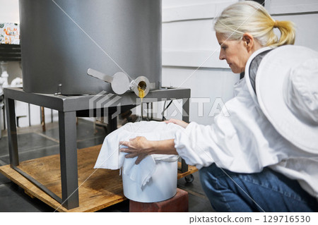 Beekeeper woman, honey production and machine in factory, workshop and organic harvesting process. Apiculture expert, natural product and working with ppe bee suit for manufacturing healthy food 129716530