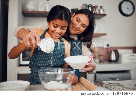 Baking, children and kitchen with a mother and daughter learning about cooking or food in their home together. Family, love and bonding with an indian woman teaching her female child how to bake Baking, children and kitchen with a mother and daughter learning about cooking or food in their home together. Family, love and bonding with an indian woman teaching her female child how to bake 129716670
