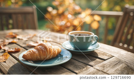 Golden Flaky Croissant and a Warm Cup of Coffee on a Sunny Outdoor Patio Table, Capturing the Cozy and Relaxing Mood of an Autumn Morning Golden Flaky Croissant and a Warm Cup of Coffee on a Sunny Outdoor Patio Table, Capturing the Cozy and Relaxing Mood of an Autumn Morning 129716690