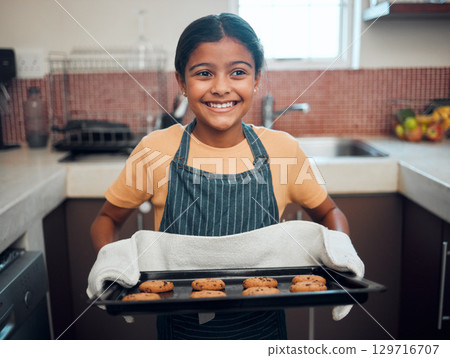 Baking, cookies and children with an indian girl cooking baked goods in the kitchen of her home alone. Food, kids and apron with a female child learning how to bake in her house in the morning 129716707