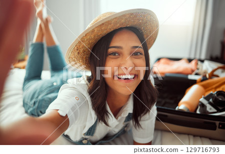 Face, travel selfie and woman packing suitcase getting ready for vacation or holiday. Portrait, relax and happy female taking pictures in hat while loading luggage on bed in preparation for trip. Face, travel selfie and woman packing suitcase getting ready for vacation or holiday. Portrait, relax and happy female taking pictures in hat while loading luggage on bed in preparation for trip. 129716793