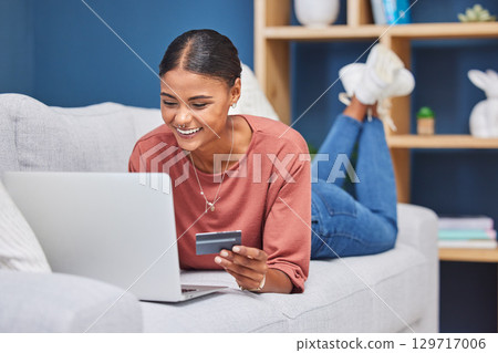 Credit card, laptop and woman relax on sofa online shopping, ecommerce website and shop fashion sale in living room. Black woman, happy customer and digital tech purchase with bank card or bank app 129717006