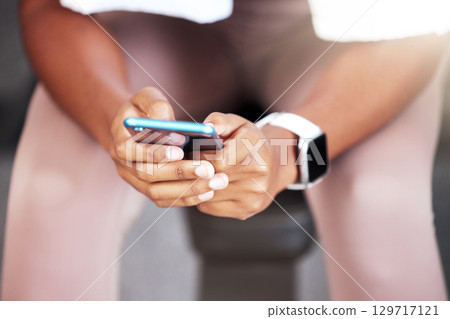Phone, hands and black woman in gym, sitting or rest at workout, training or self care with smartwatch. Smartphone texting, social media app or woman in fitness studio on break for body wellness 129717121