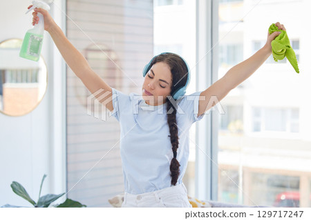 Woman cleaning, dancing and listening to music with headphones while holding cloth and detergent to clean with energy, fun and audio podcast. Female cleaner or maid working in a house or apartment 129717247