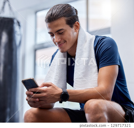 Fitness, phone and man relax in gym tracking workout, exercise or progress on app. Tech, sports and happy male with towel and mobile smartphone for internet browsing, text messaging or social media. 129717321