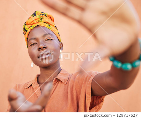 Black woman, face portrait and hands frame for fashion aesthetic, african culture and turban in studio with orange background. Nigeria, cosmetics makeup and traditional head scarf or playful gesture 129717627