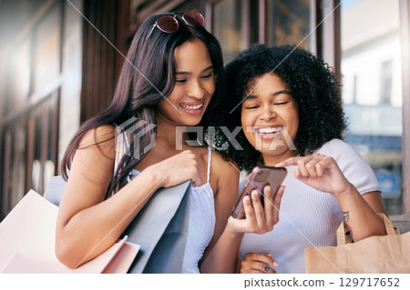 Friends, shopping and phone at a mall in the city while happy and excited about a sale online with discount and savings. Females in Milan with consumer bags and smartphone for banking notification 129717652