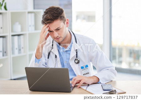 Doctor, laptop and stress headache about bad news or diagnosis for medical professional in his office. Hospital, clinic and male gp specialist reading email and feeling upset with a migraine 129717837