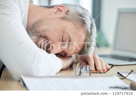 Burnout, sleeping and tired business man at his desk for financial report, audit or tax documents with time management fail or mental health risk. Fatigue, depression and sad businessman in workplace Burnout, sleeping and tired business man at his desk for financial report, audit or tax documents with time management fail or mental health risk. Fatigue, depression and sad businessman in workplace 129717918