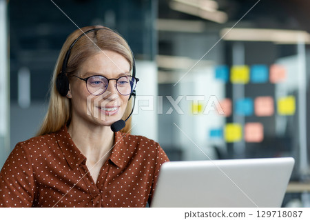 A confident businesswoman in glasses and headset reviewing tasks on a laptop, collaborating remotely. 129718087