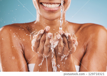 Water splash, hands and black woman with wellness, skincare and smile. Wet, liquid drops and young female with body care, health and on blue studio background for natural beauty, smooth or clear skin Water splash, hands and black woman with wellness, skincare and smile. Wet, liquid drops and young female with body care, health and on blue studio background for natural beauty, smooth or clear skin 129718321