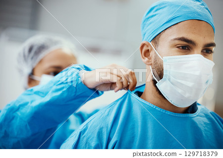 Surgeon, doctor or medical man with nurse helping with clean scrubs and face mask for surgery, healthcare and safety in theatre. Emergency, ppe and operation staff in a hospital for life insurance Surgeon, doctor or medical man with nurse helping with clean scrubs and face mask for surgery, healthcare and safety in theatre. Emergency, ppe and operation staff in a hospital for life insurance 129718379