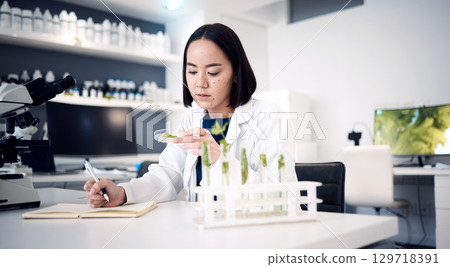 Scientist, plant and medical research with ecology, green leave and nature medicine while writing notes in laboratory. Asian woman doctor with petri dish for innovation, development and analysis 129718391