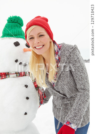 Portrait, winter and woman with a snowman during Christmas, outside in the snow in the UK. Face, front and female with snow man in xmas or festive season to celebrate and have fun with a smile 129718423