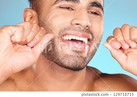Face, dental and man floss teeth in studio isolated on blue background. Veneers, invisalign and male model from Brazil flossing, cleaning for wellness or mouth hygiene, oral care and tooth health. Face, dental and man floss teeth in studio isolated on blue background. Veneers, invisalign and male model from Brazil flossing, cleaning for wellness or mouth hygiene, oral care and tooth health. 129718715