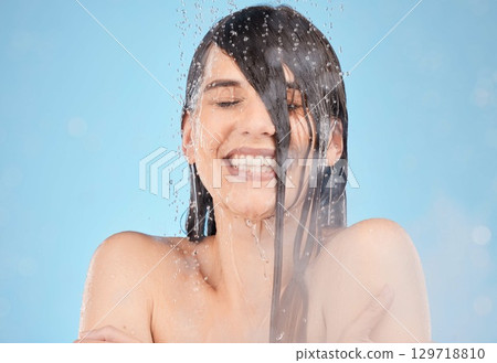Water, steam and cleaning with a woman in the shower in studio on a blue background for hygiene or hydration. Skincare, relax and smile with a model female washing her face in the bathroom for health Water, steam and cleaning with a woman in the shower in studio on a blue background for hygiene or hydration. Skincare, relax and smile with a model female washing her face in the bathroom for health 129718810
