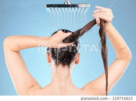 Shower head, woman and washing hair on blue background for healthy skincare, beauty and wellness in studio. Back of female model cleaning body, long hair and scalp with water splash, tap and bathroom 129718823