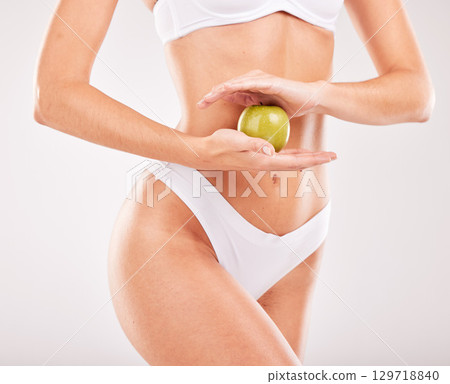 Wellness, diet and hands with apple for slim body, self care and healthy lifestyle on white background studio. Fitness, exercise and abdomen of woman with fruit for vitamins, nutrition and weightloss Wellness, diet and hands with apple for slim body, self care and healthy lifestyle on white background studio. Fitness, exercise and abdomen of woman with fruit for vitamins, nutrition and weightloss 129718840