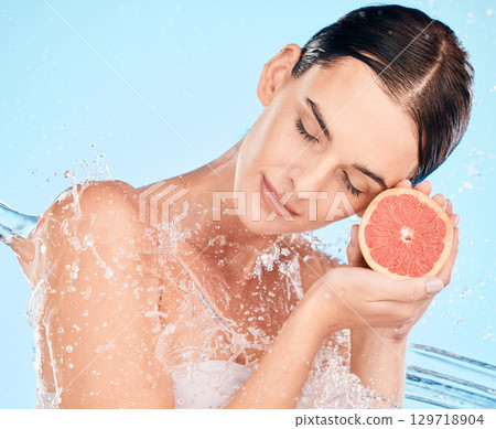 Beauty, splash and water with a woman holding fruit for health, skincare and wellness on a blue studio background. Clean, shower and cosmetics with a grapefruit for vitamin c skin care and bodycare Beauty, splash and water with a woman holding fruit for health, skincare and wellness on a blue studio background. Clean, shower and cosmetics with a grapefruit for vitamin c skin care and bodycare 129718904