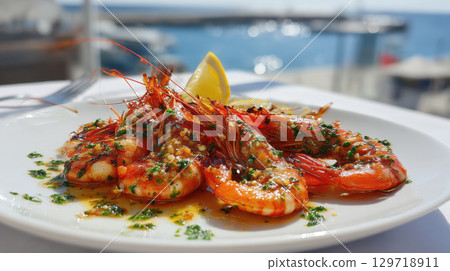 A perfectly cooked plate of grilled prawns is presented on a white plate, topped with fresh herbs and a savory sauce. The background shows a stunning seaview, creating a gourmet dining experience 129718911