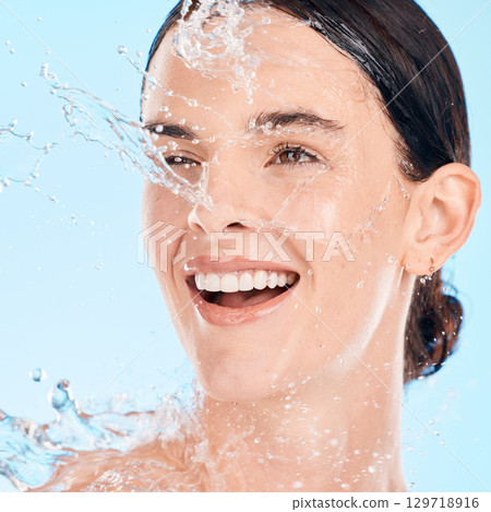 Face, woman and water for skincare, natural beauty and organic facial against blue studio background. Young female, girl and liquid drops for hygiene, detox and wet for washing, shower and smile. 129718916