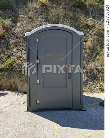 This plastic toilet is strategically located beside a mountainside, catering to hikers and outdoor enthusiasts. Its placement ensures convenient sanitation access in a natural setting. 129718924