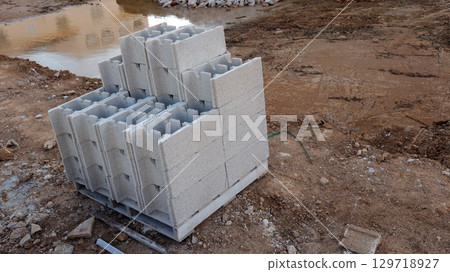Excavation has commenced for a new pool, featuring a pit that's been prepared for building. Hollow bricks are stacked neatly on pallets, ready for use in the construction process. 129718927