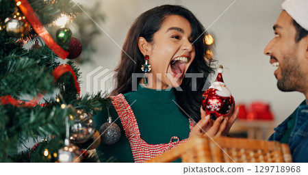 Christmas, tree and surprise with couple and bauble for festive season, tradition and decoration. Xmas, holiday cheer and celebration with man and woman in living room of home for happy and ornament Christmas, tree and surprise with couple and bauble for festive season, tradition and decoration. Xmas, holiday cheer and celebration with man and woman in living room of home for happy and ornament 129718968