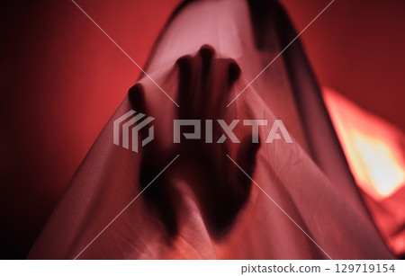 Hand, fabric and red with a person under a sheet in a bedroom or studio on a red background for psychology. Hands, silhouette and shadow with an adult struggling with mental health, anxiety or fear 129719154