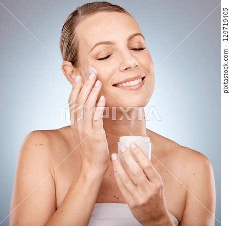 Skincare, beauty and cream on face, woman on studio background for skin and body care. Happy, clean and fresh bathroom beauty routine for model. Sun protection application of anti aging sunscreen. 129719405