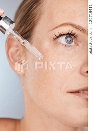 Face, skincare and serum with a model woman in studio on a gray background to promote a cosmetic product. Facial, beauty and antiaging with a female applying oil to her skin for natural cosmetology 129719411