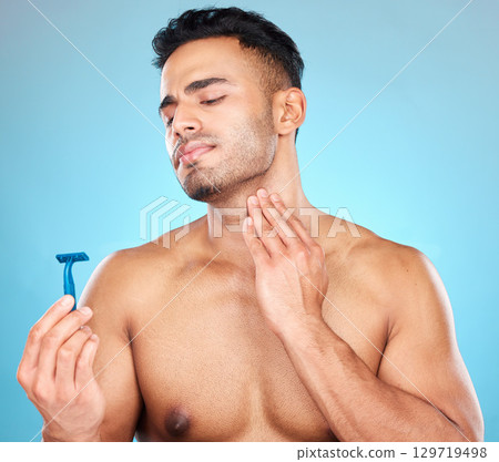 Skincare, shaving and man with razor in studio on blue background for wellness, beauty and self care. Grooming, facial treatment and male face with worry, concern and anxiety to shave sensitive skin 129719498