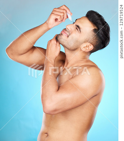Health, vision and man with eye drops for allergy on blue background for wellness, eye and optical care. Optometry, healthcare and young male apply liquid, drops and medicine in eyes for contact lens 129719524