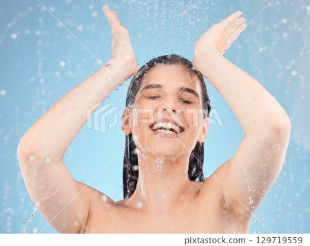 Woman, showering and water splash on blue background in studio for healthcare wellness, hygiene maintenance or skincare grooming. Smile, happy or beauty model in wet cleaning in spa or house bathroom 129719559