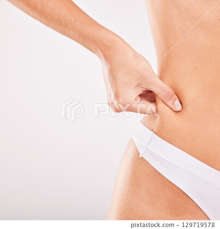 Woman hand, body weight and loss for liposuction, tummy tuck and abdomen in underwear in grey studio background. Cellulite and fat with a female model with healthy lifestyle and diet for stomach loss Woman hand, body weight and loss for liposuction, tummy tuck and abdomen in underwear in grey studio background. Cellulite and fat with a female model with healthy lifestyle and diet for stomach loss 129719578