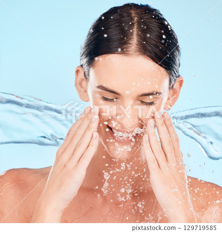 Woman, face and skincare with splash in studio for beauty, wellness and self care by blue background. Water, model and smile with moisturizer, cleaning and happy for natural cosmetics for dermatology Woman, face and skincare with splash in studio for beauty, wellness and self care by blue background. Water, model and smile with moisturizer, cleaning and happy for natural cosmetics for dermatology 129719585