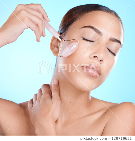 Beauty, face and roller tool for cosmetic luxury skincare health on blue studio background. Facial massage accessory, anti aging cosmetics routine and clean skin wellness with a healthy facial glow Beauty, face and roller tool for cosmetic luxury skincare health on blue studio background. Facial massage accessory, anti aging cosmetics routine and clean skin wellness with a healthy facial glow 129719631