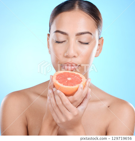 Face, skincare and woman with grapefruit and eyes closed in studio isolated on a blue background. Wellness, food or female model holding healthy fruit for natural vitamin c, nutrition or healthy skin 129719656