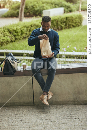 Black business man on a lunch break in the city, sitting and eating a meal or sandwich in a brown paper bag. Hungry worker relaxing with a tasty snack, food on the go for a professional entrepreneur Black business man on a lunch break in the city, sitting and eating a meal or sandwich in a brown paper bag. Hungry worker relaxing with a tasty snack, food on the go for a professional entrepreneur 129719800