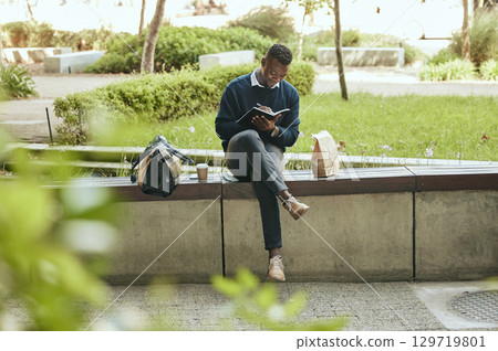 Businessman in park writing in notebook planning in his work schedule, journal or diary outdoors. Smart entrepreneur, corporate or professional employee on his lunch, coffee and tea break in nature 129719801