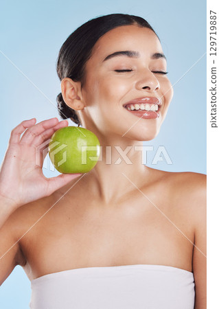 Skincare, healthcare beauty and woman with apple in hand with sweet fruit, health and dental teeth against a blue studio background. Portrait of a female in healthy natural skin and diet with smile. 129719887