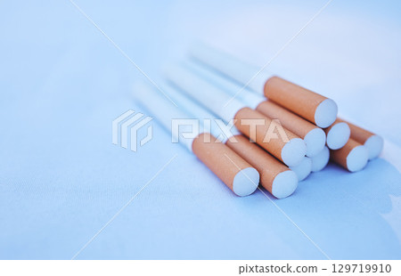 Cigarette, cancer and smoke with a tobacco product on the ground against a blue background to promote awareness. Smoking, toxic and addiction with cigarettes in a pile or stack on the floor Cigarette, cancer and smoke with a tobacco product on the ground against a blue background to promote awareness. Smoking, toxic and addiction with cigarettes in a pile or stack on the floor 129719910