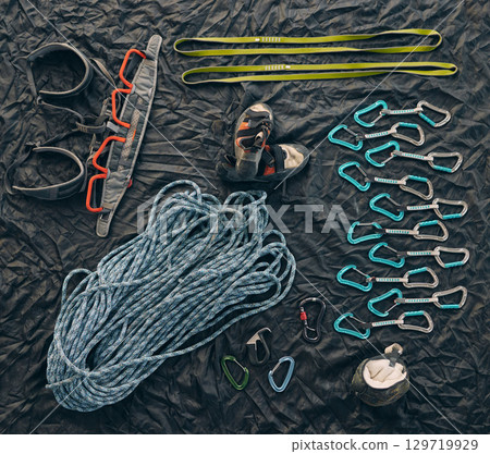 Rock or mountain climbing equipment or tools against dark background with a carabiner hook, rope for safety and security. Extreme sport object organized on floor or ground with sportswear and shoes 129719929