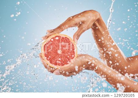 Hands, water splash and grapefruit cosmetic skincare for vitamin c nutrition, citrus health treatment and natural wellness. Healthy skin hygiene, advertising hydration and a blue studio background 129720105