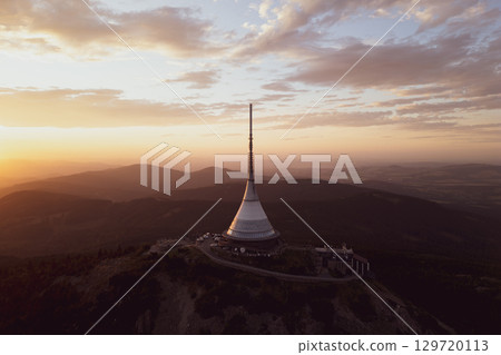 Jested Mountain Hotel showcases modern architecture under a vibrant sunset. Perched atop the mountain, it offers breathtaking views of the surrounding landscape during a serene evening. 129720113