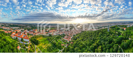 A breathtaking sunrise illuminates the sky above Prague, highlighting the Vltava River and Prague Castle. The lush greenery of Petrin Hill contrasts beautifully with the vibrant cityscape. 129720148