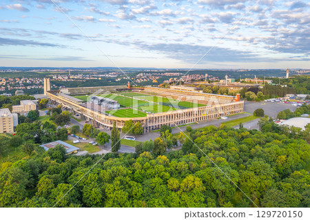 Great Strahov Stadium, located in Prague, showcases its vast open field amidst lush greenery. Surrounding hills and urban landscapes add to the stadium's impressive views during late afternoon light. 129720150