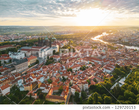 Golden sunlight bathes Prague Castle and its surroundings at dawn, casting long shadows across the red rooftops of the historic city. A moment of tranquility before a busy day begins. Golden sunlight bathes Prague Castle and its surroundings at dawn, casting long shadows across the red rooftops of the historic city. A moment of tranquility before a busy day begins. 129720153