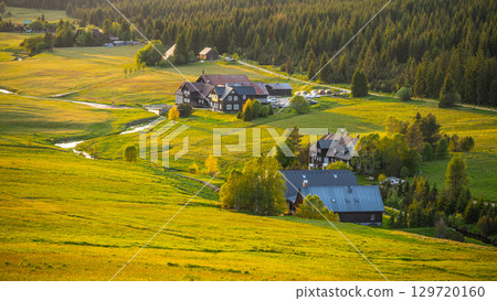 Evening light casts a warm glow over Jizerka Village in the Jizera Mountains. The tranquil landscape features fields, forests, and quaint houses surrounded by nature's beauty. Evening light casts a warm glow over Jizerka Village in the Jizera Mountains. The tranquil landscape features fields, forests, and quaint houses surrounded by nature's beauty. 129720160