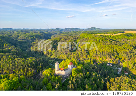 Golden evening light bathes Kokorin Castle as it rests amid dense forests and rolling hills in Czechia. An aerial perspective reveals the castle's stunning architecture and natural beauty. 129720180